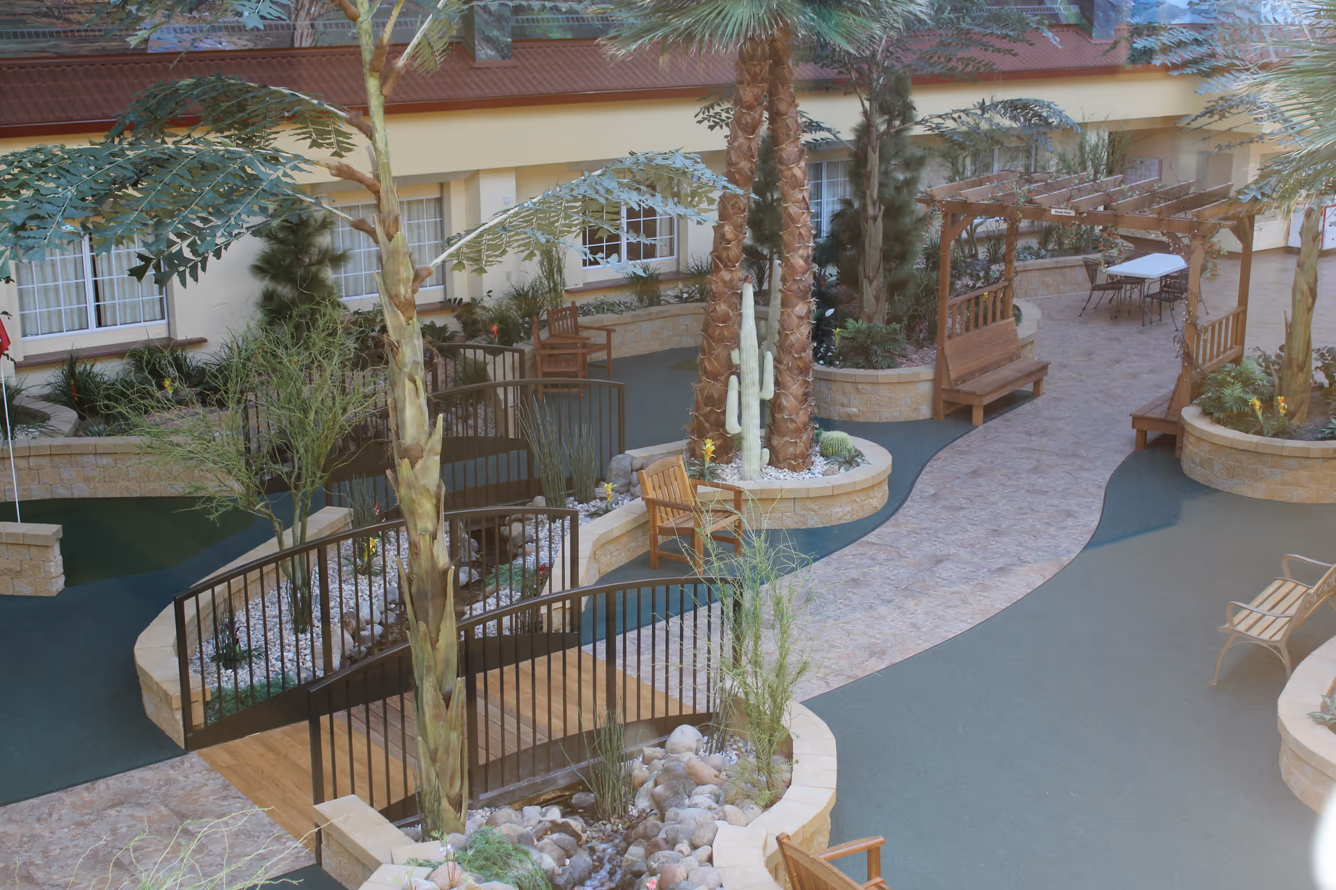 Indoor courtyard with palm trees, winding walkways, benches, pergola and seating areas.