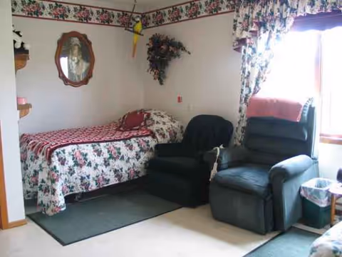 Cozy bedroom in a senior facility with floral bedspread, two recliners, and floral curtains.