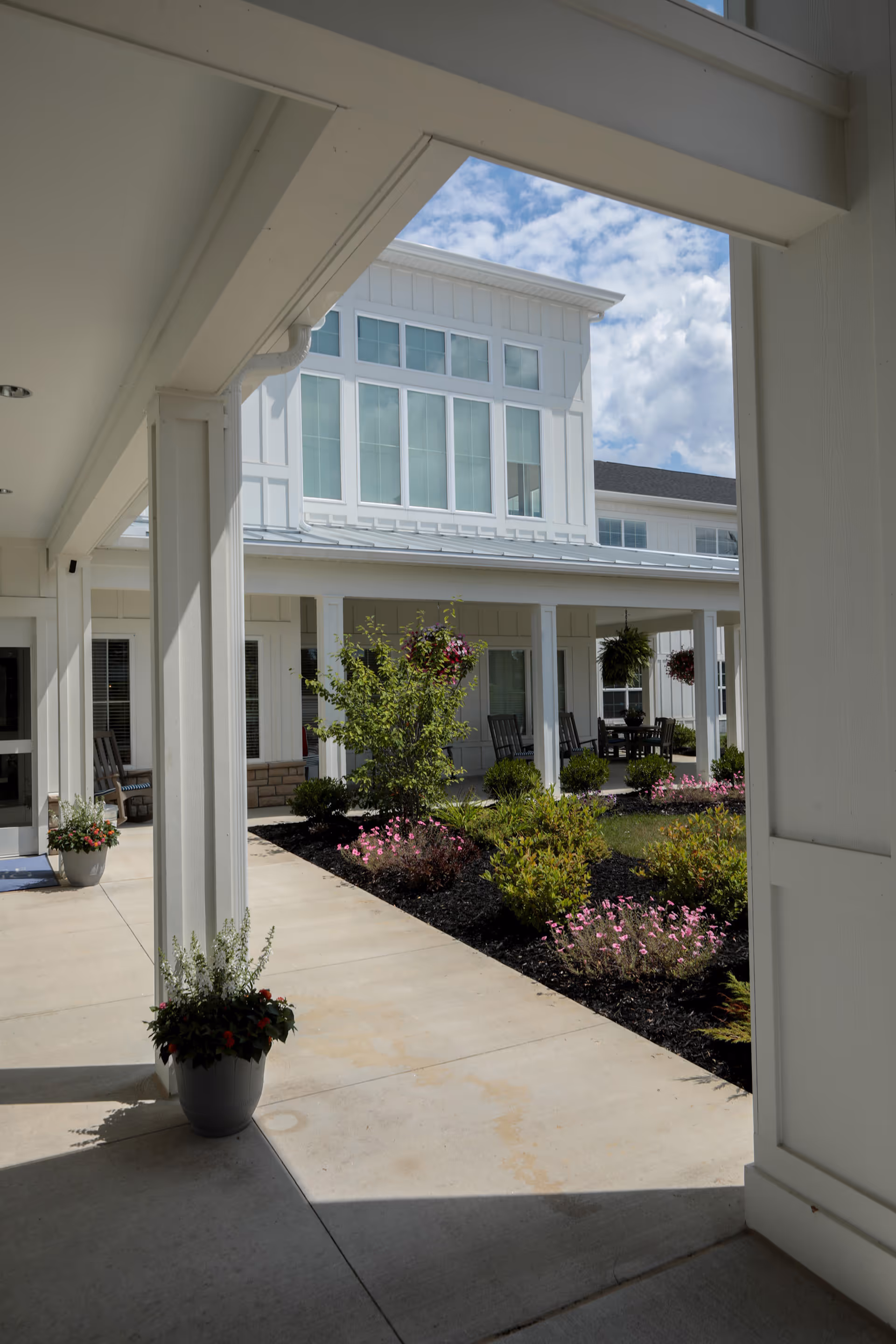 Covered porch and walkway overlooking a landscaped courtyard and a white multi-story senior living building.