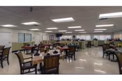 Large institutional dining room with multiple set tables and chairs under fluorescent lighting.