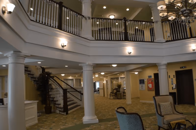 Two-story assisted living lobby with columns, balcony railing, staircase, and seating area.