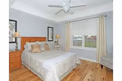Bright bedroom with a made bed, wooden nightstands, a ceiling fan, and a window overlooking a fenced yard.