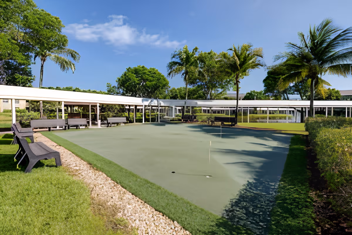 Outdoor putting green with benches, covered walkways and palm trees under a blue sky.