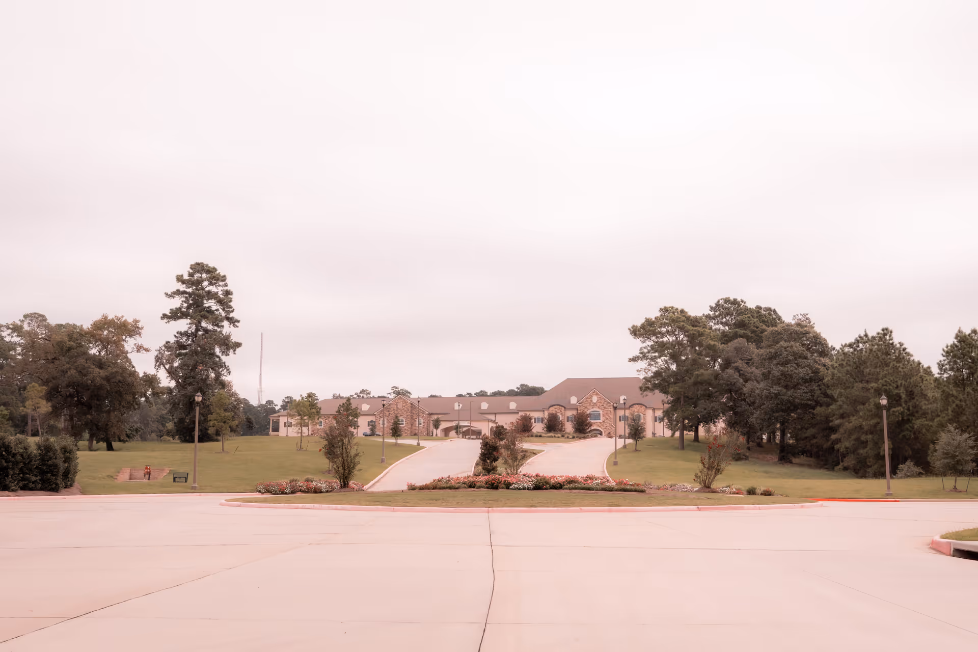 Wide view of a single-story brick building set back behind a circular driveway with landscaped lawns and trees.