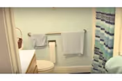 Small bathroom with a toilet, sink vanity, towel racks, and a striped shower curtain against light green walls.