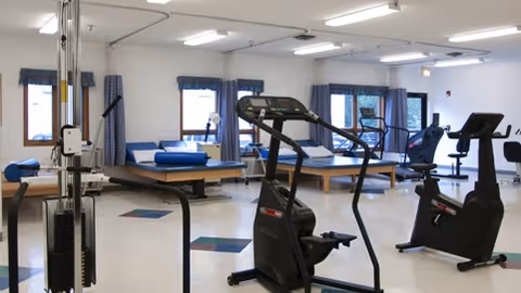 Bright rehabilitation gym with exercise bikes, treadmills, and therapy tables in a large room.