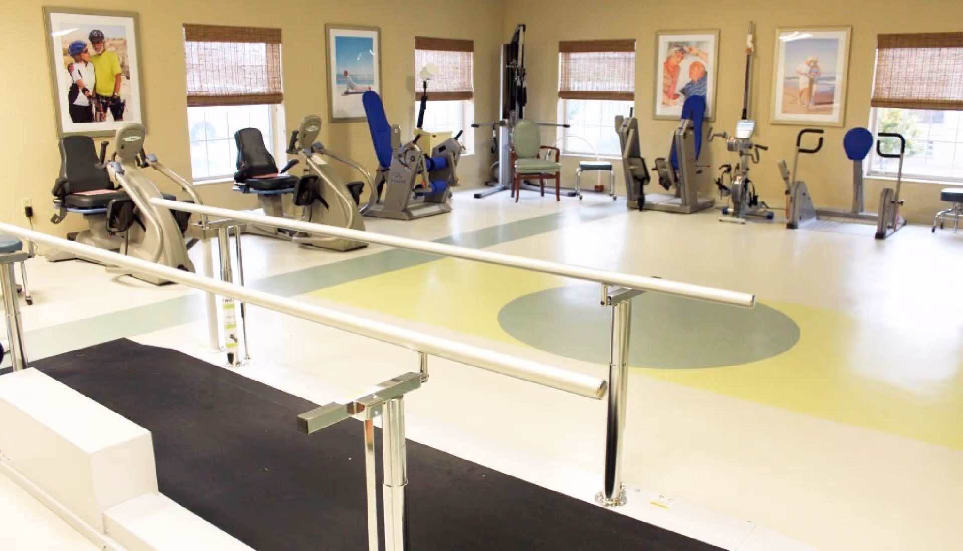 Rehabilitation gym with parallel walking bars, exercise machines and stationary bikes in a bright therapy room.