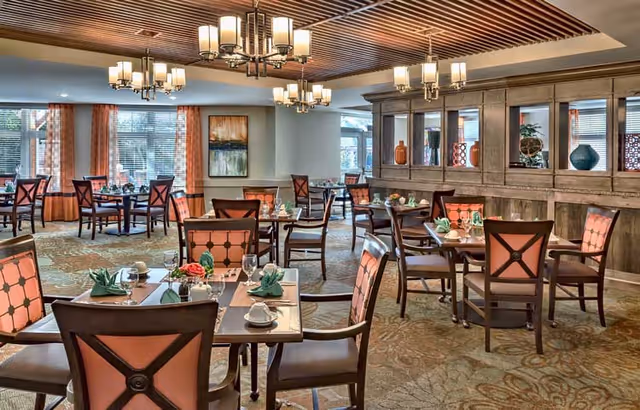 Well-appointed dining room with multiple set tables and upholstered chairs under decorative chandeliers.