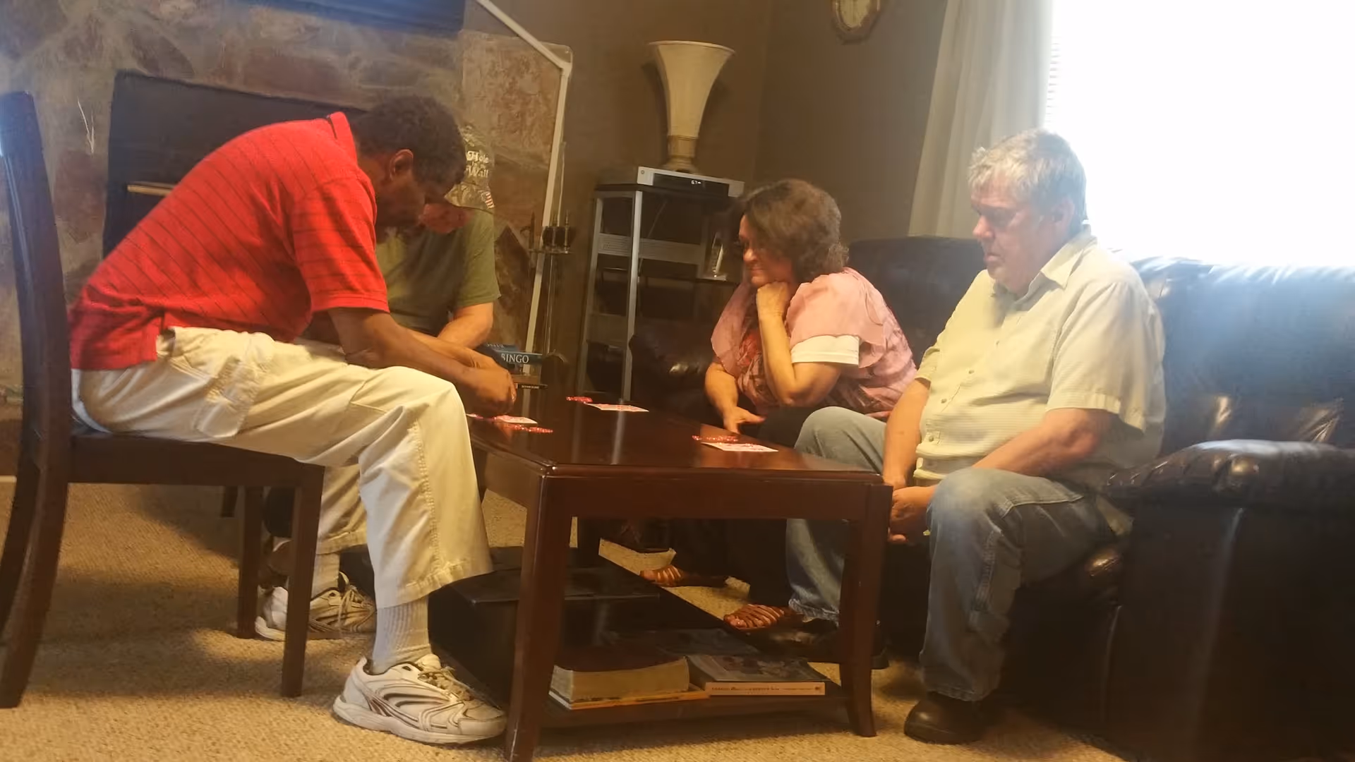 Four adults sit around a coffee table in a living room playing cards.