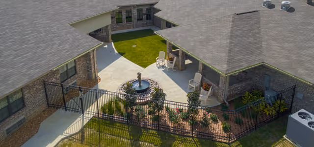 Aerial view of a gated courtyard with a central fountain, walkways, seating, and landscaped beds between brick buildings.