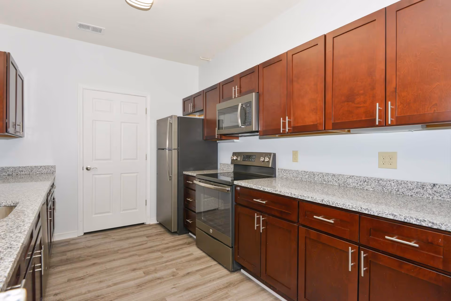 Modern kitchen with stainless steel refrigerator, stove, and microwave, granite countertops and dark wood cabinets.