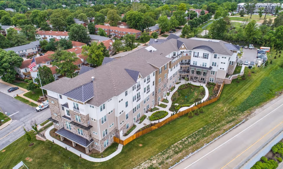Aerial view of a multi-story senior living building with a landscaped courtyard, parking area, and surrounding neighborhood.