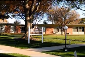 Exterior view of a single-story brick building with a sign reading 'Good Neighbor Society' in front, surrounded by trees with autumn foliage and a well-maintained lawn.