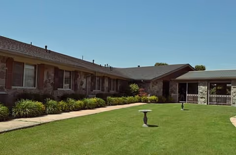 Single-story nursing facility with brick exterior and a green courtyard lawn.