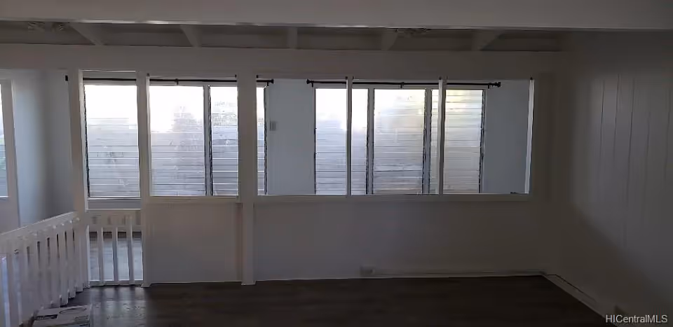 Empty interior room with white walls, multiple windows with horizontal blinds, a white railing on the left side, and dark wood flooring.