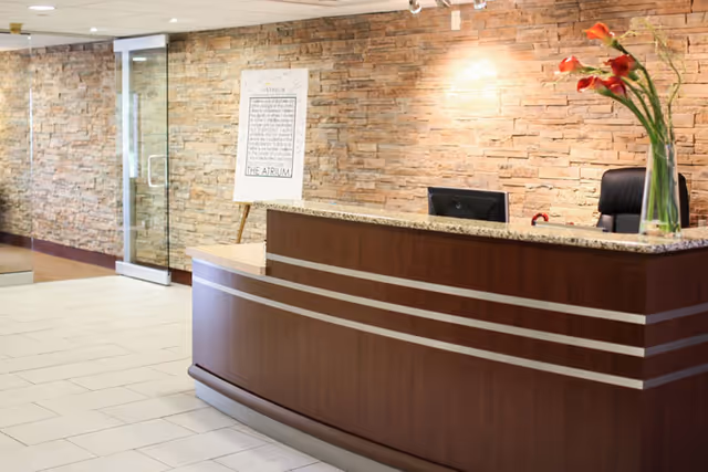 Reception desk with granite countertop, vase of red flowers, and a stone accent wall in a facility lobby.