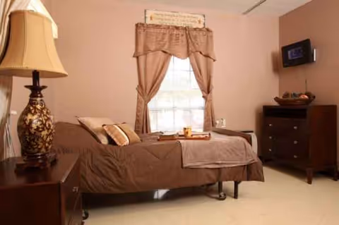 A cozy bedroom in a senior living facility with bed, dresser, and window.
