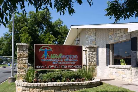 Front exterior of Wellington Rehabilitation and Healthcare with a sign and landscaped entry.