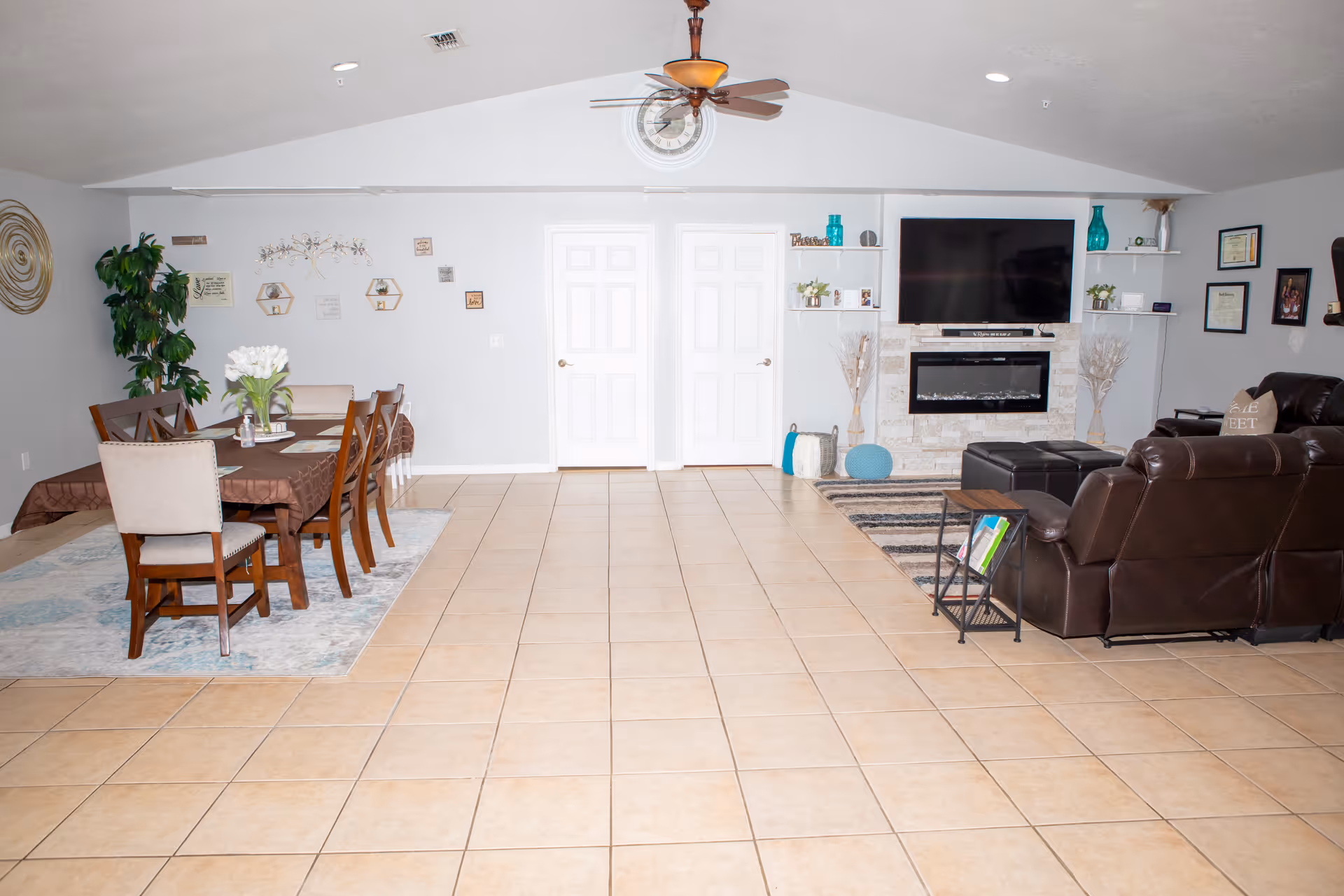 Spacious open living and dining area with a tiled floor, dining table on the left and leather sofas, TV and fireplace on the right.
