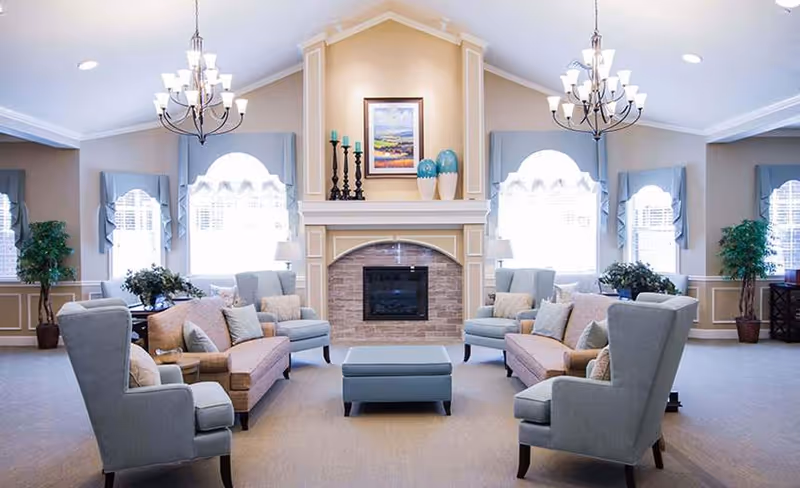 Communal living room with sofas and armchairs arranged around a central fireplace under chandeliers.