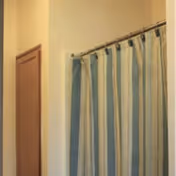 Striped blue and green shower curtain next to a wooden door and cream-colored walls.