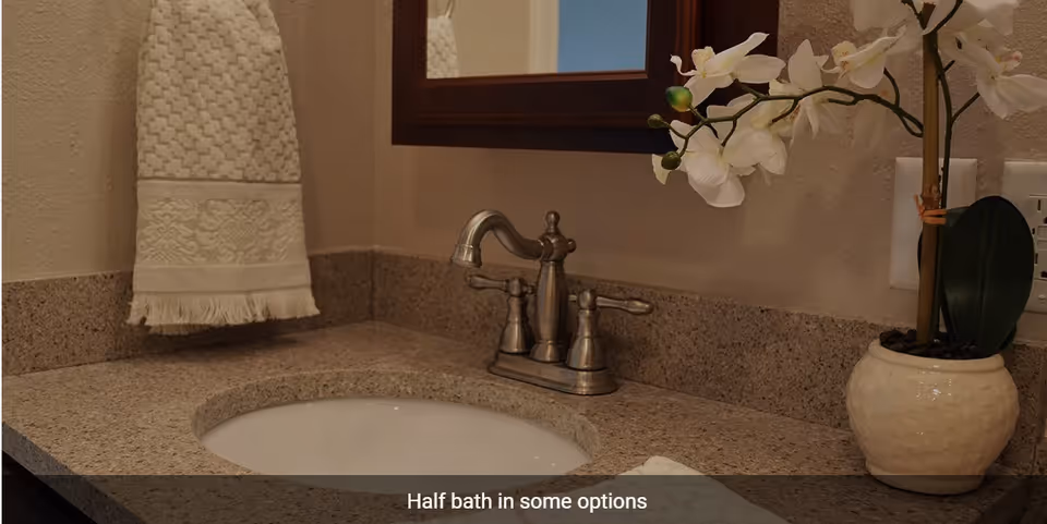 A bathroom sink with a granite countertop, a silver faucet, a white towel hanging on the wall, and a white orchid plant in a ceramic pot next to the sink.