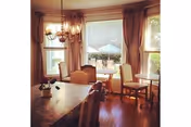 Bright dining room with a chandelier, wooden table and chairs in front of a large window overlooking a patio with an umbrella.