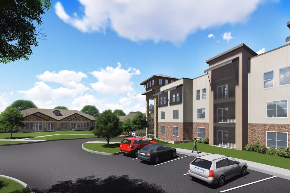 Exterior view of a senior living facility named Watermere at the Preserve, showing a three-story building with balconies, a parking lot with several cars, a person walking on the sidewalk, green lawns, trees, and a partly cloudy blue sky.