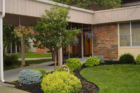 Covered entrance to a healthcare building with a brick facade, walkway, and neatly landscaped shrubs.