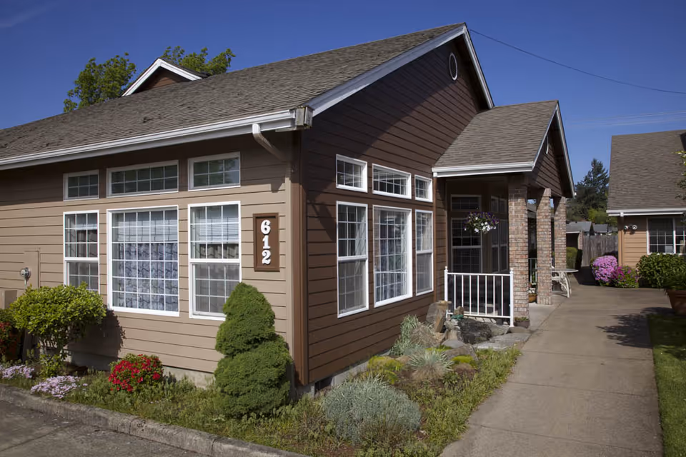 Single-story brown residential building with large windows, a porch entrance marked 612, and a paved walkway with landscaping.