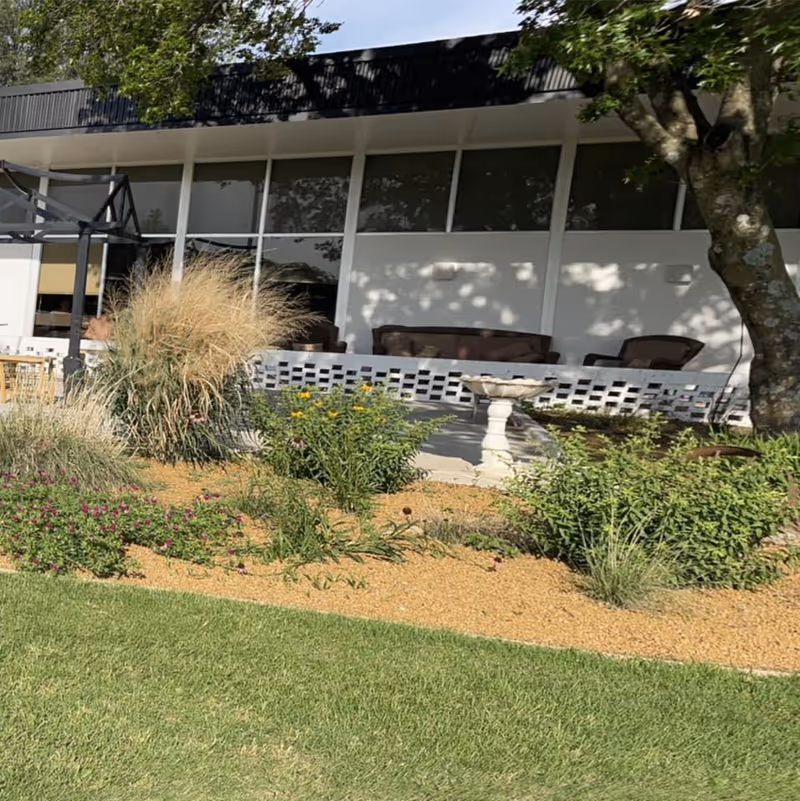 Patio and landscaped front lawn with a birdbath, plants and outdoor seating in front of a single-story building.
