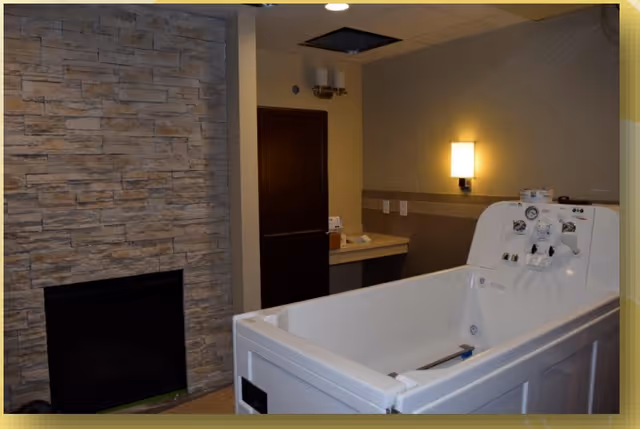 Room with a white walk-in therapeutic bathtub, stone fireplace, and a countertop sink area.