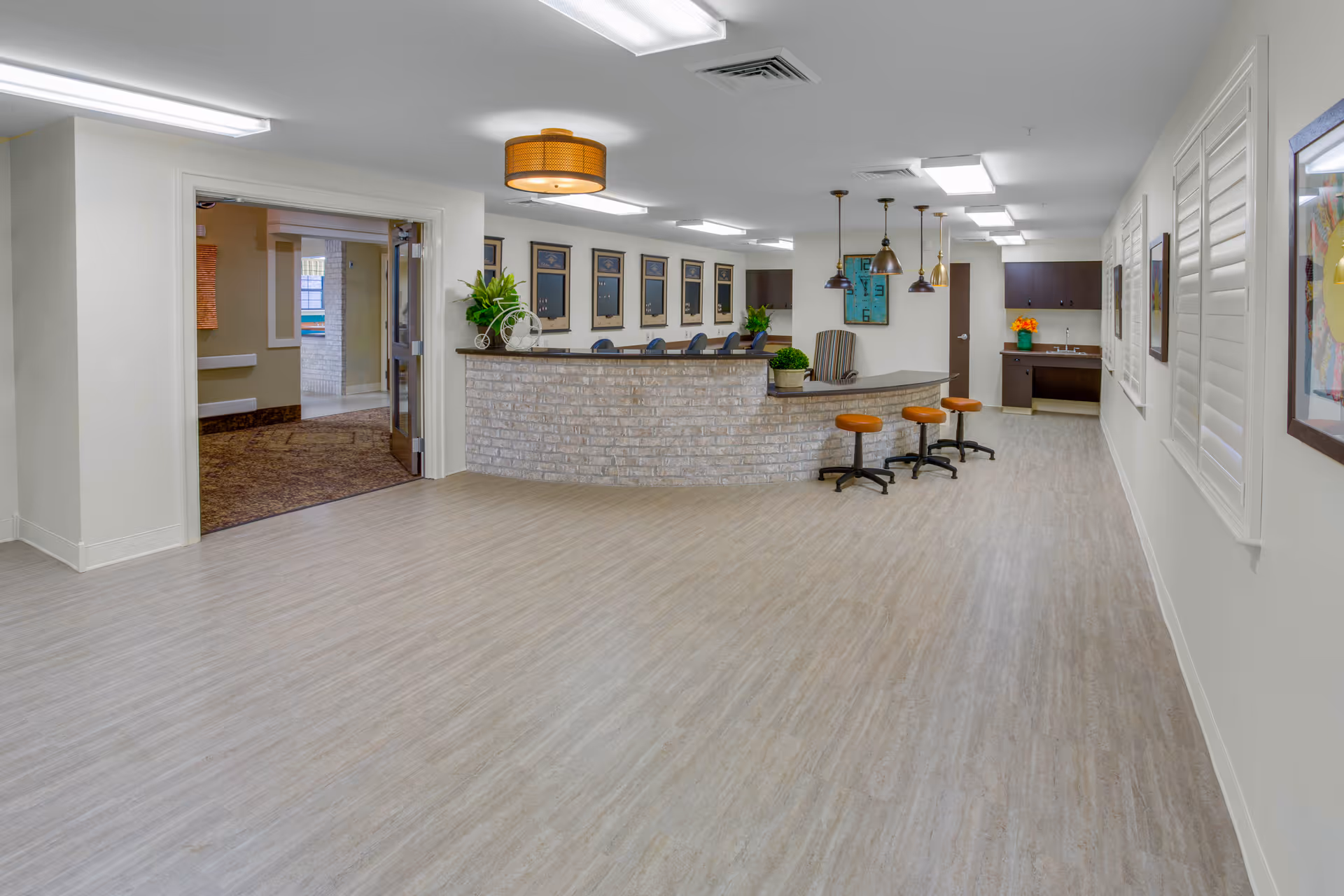 Bright interior reception area with a curved brick front desk, bar stools, pendant lights, and a wide laminate-floored hallway.