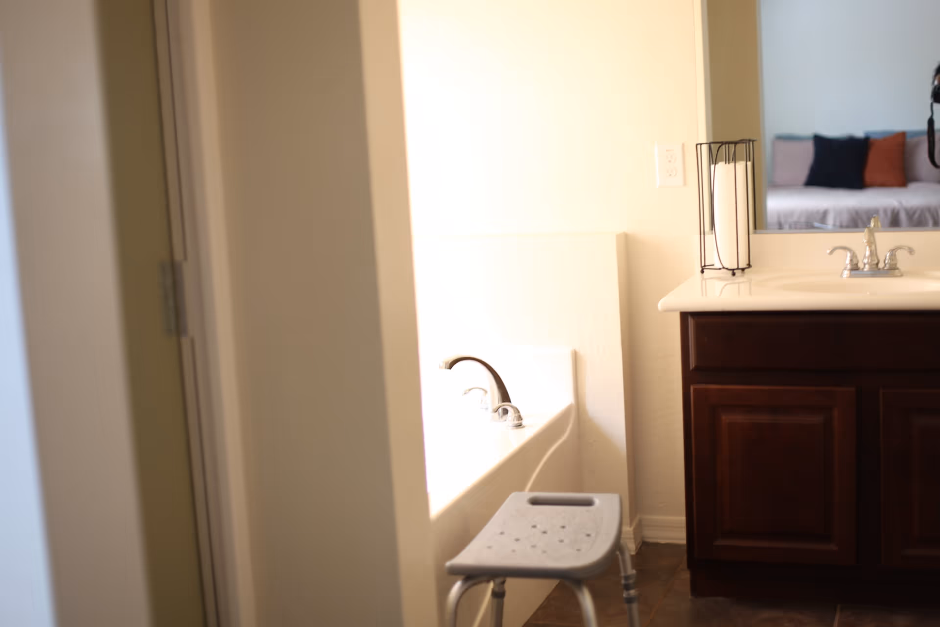 Bathroom showing a bathtub with a faucet, a sink vanity with dark wood cabinets and mirror, and a small shower stool.