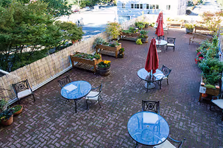 Outdoor brick patio with blue round tables, chairs, and red umbrellas.