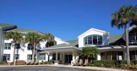 Modern senior living facility exterior with palm trees and porte-cochere entrance