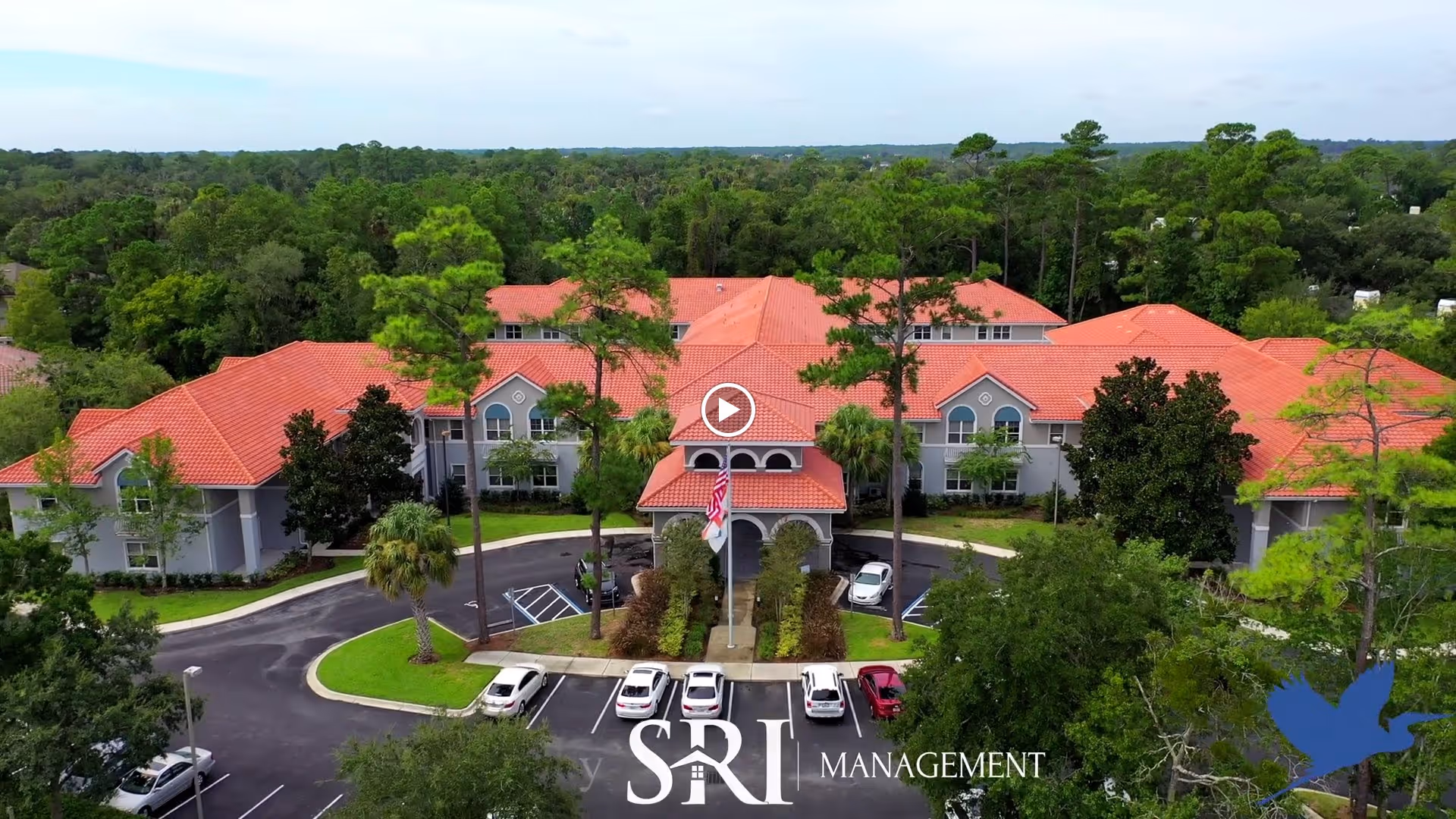 Aerial view of The Cove at Marsh Landing showing a red-tiled roof building entrance surrounded by trees and parked cars.