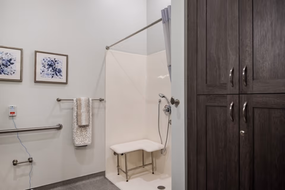Accessible bathroom with a walk-in shower and bench, grab bars, towel rack, floral wall art, and dark wood storage cabinets.