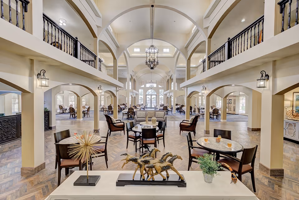 Spacious two-story communal lounge with vaulted arches, multiple seating areas and tables arranged under chandeliers.