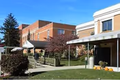 Brick senior living facility exterior showing a covered entrance, walkway, landscaping and pumpkins on the lawn.