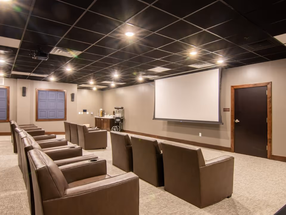 Small screening room with rows of brown leather recliners facing a large projection screen and a concession cart against the back wall.