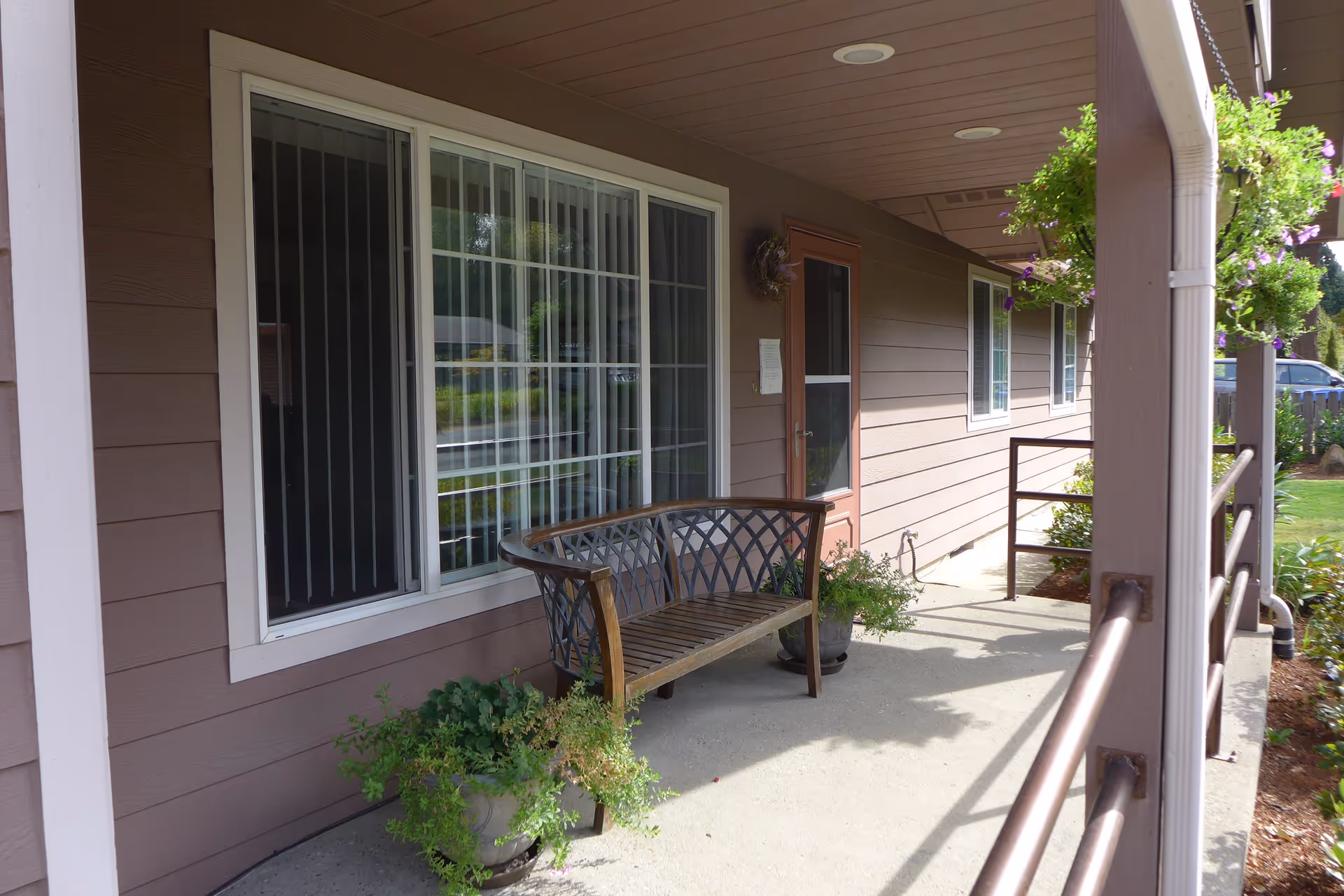 Covered front porch with a bench, potted plants, windows and an entry door.