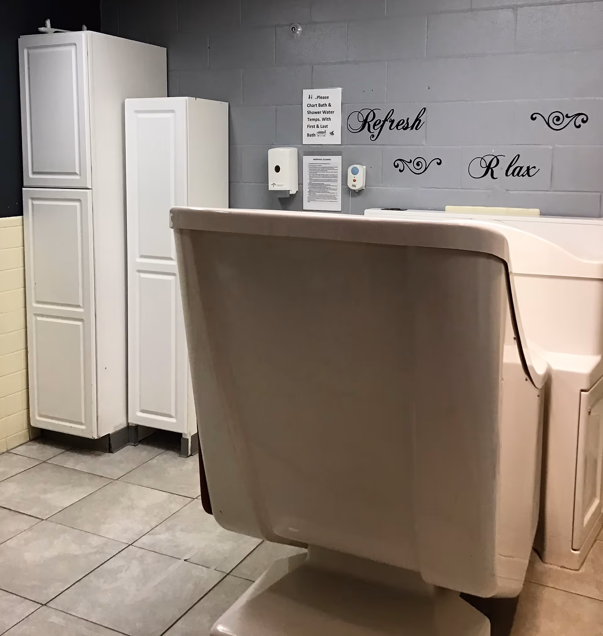 Walk-in bathtub in a tiled bathing room with white storage cabinets and 'Refresh' and 'Relax' wall decals.