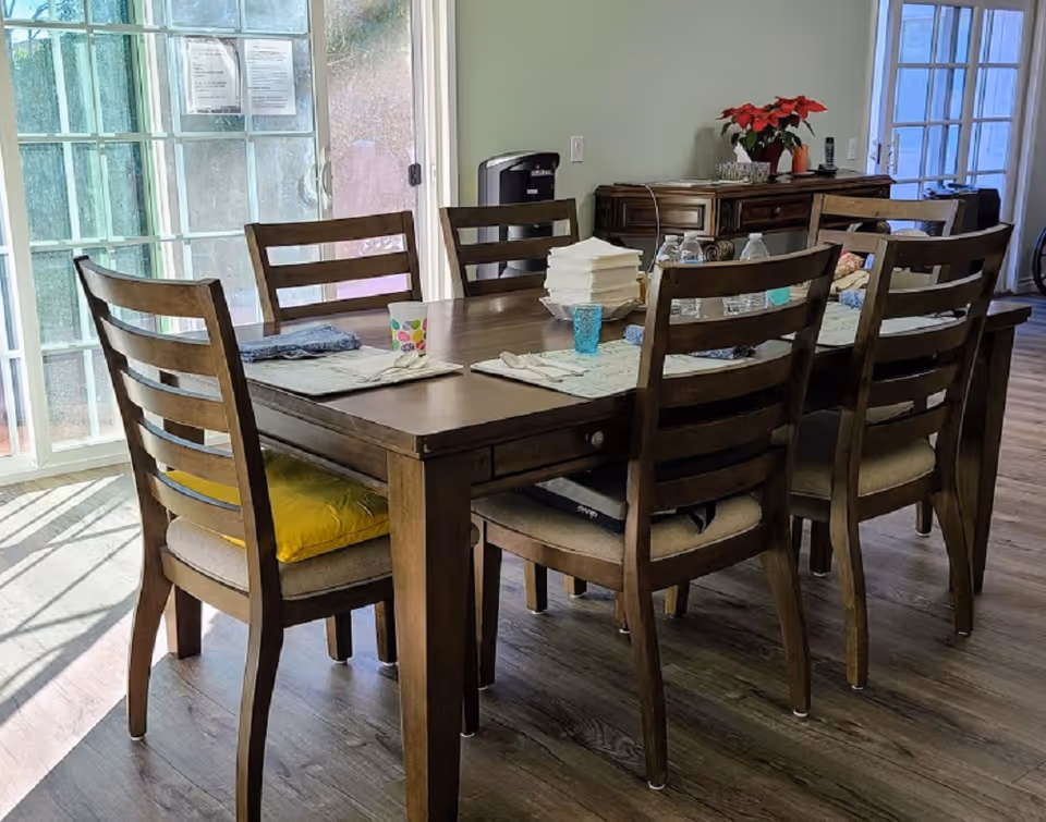 Wooden dining table with six chairs set in a bright dining area near sliding glass doors.