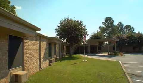 Exterior view of a brick senior living facility with a parking lot and green lawn.
