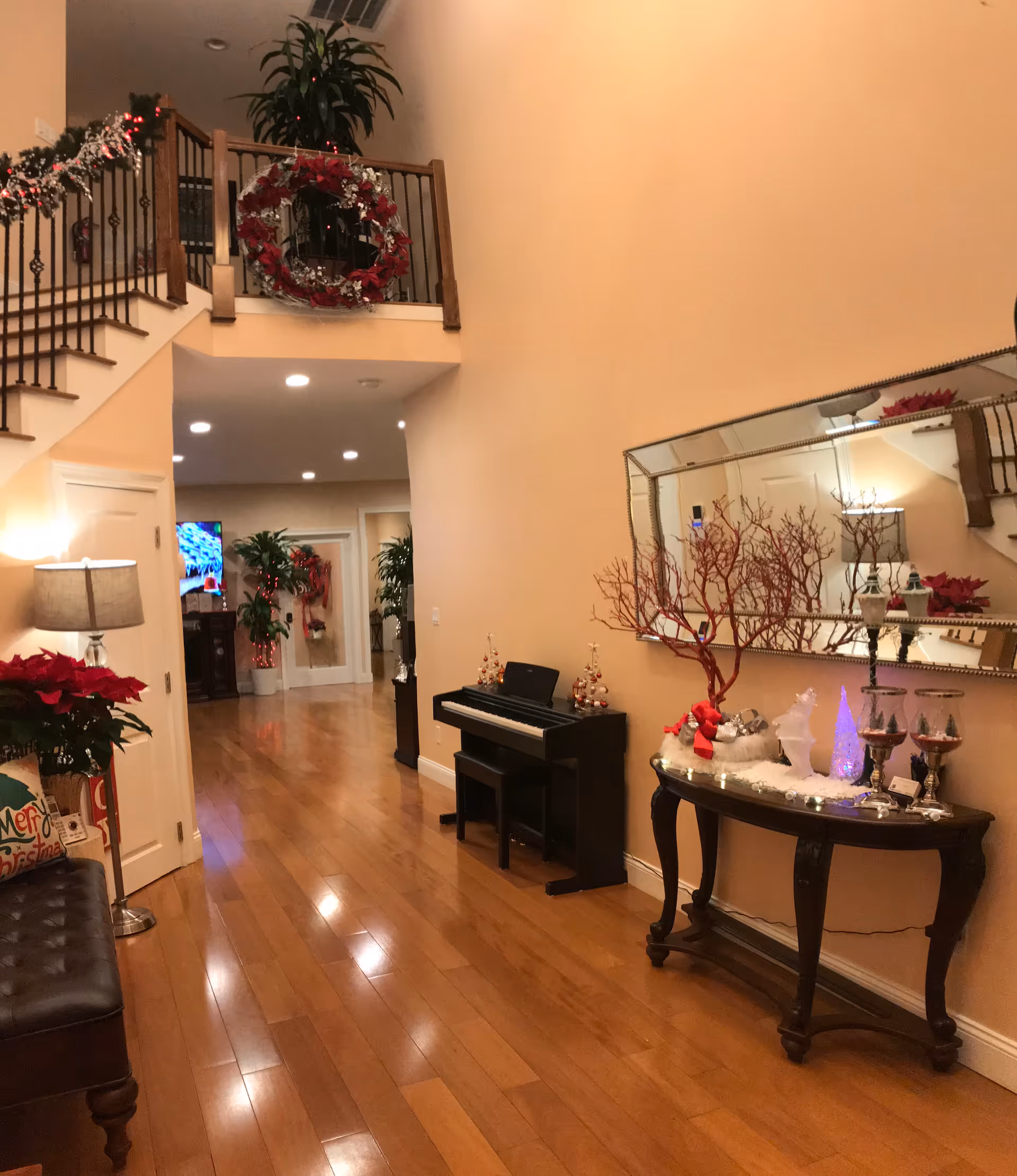 Decorated foyer/hallway with a staircase, small piano, console table and mirror, and holiday decorations.
