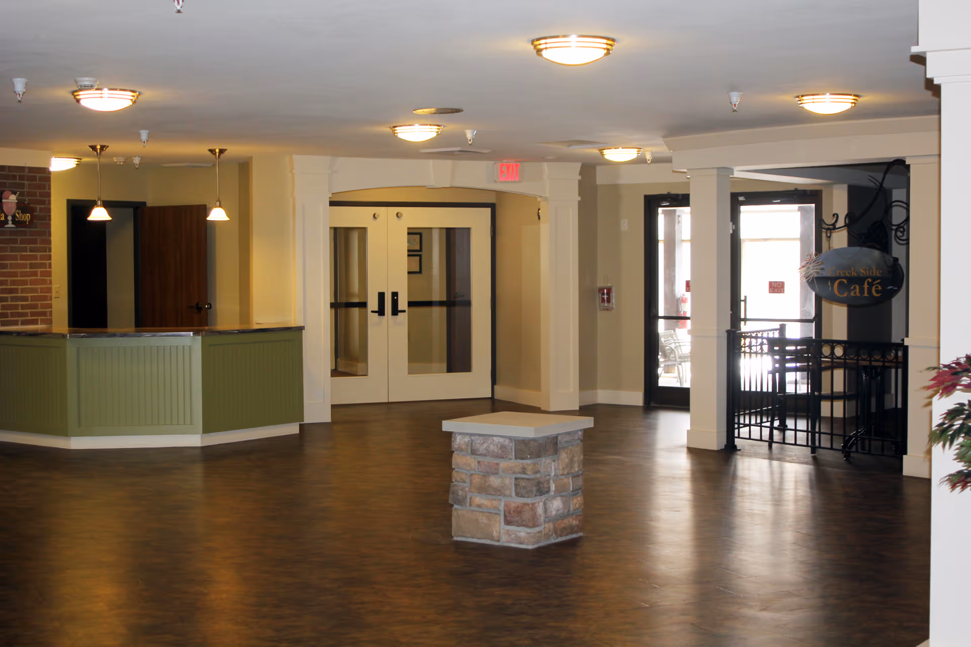 Spacious interior lobby with a reception desk, double glass doors, a small stone pedestal, and a café entrance sign.