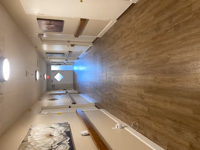 Long indoor hallway with wood-look flooring, handrails, doors and wall art leading to an exit door.