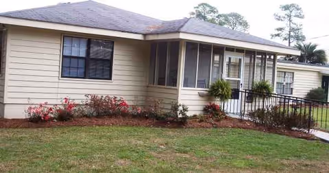 Front view of Tebeau House Personal Care Home: single-story beige building with landscaped yard.