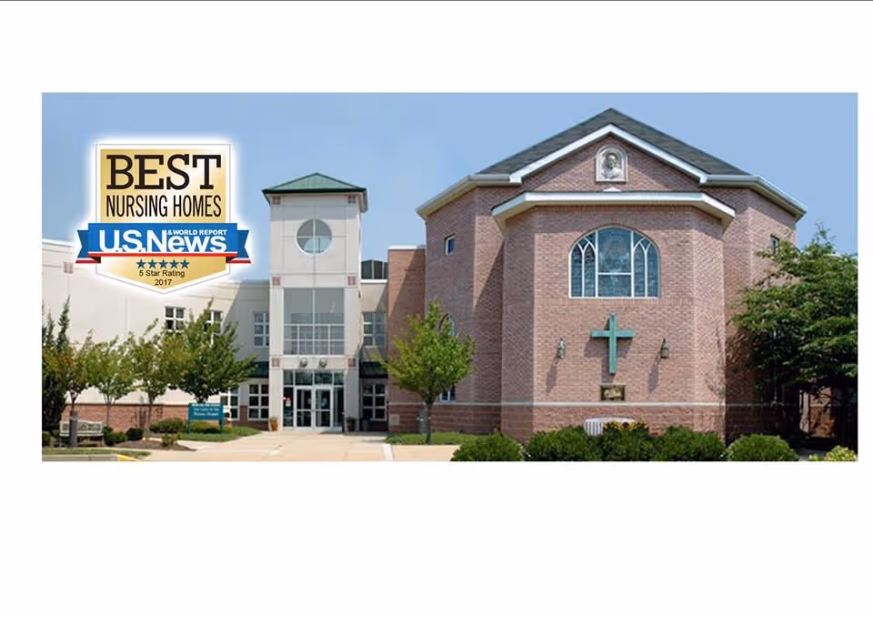 Exterior front view of a brick building with a cross mounted on the wall and a large arched window above it. The entrance has glass doors and is flanked by trees and shrubs. A badge on the left side of the image reads 'Best Nursing Homes U.S. News 5 Star Rating 2017'.